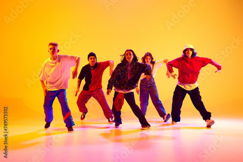 Urban dance crew in casual outfits in mid-dance in neon light against gradient colorful studio background. Concept of hobby, sport, fashion and style, action, youth culture, music and dance.