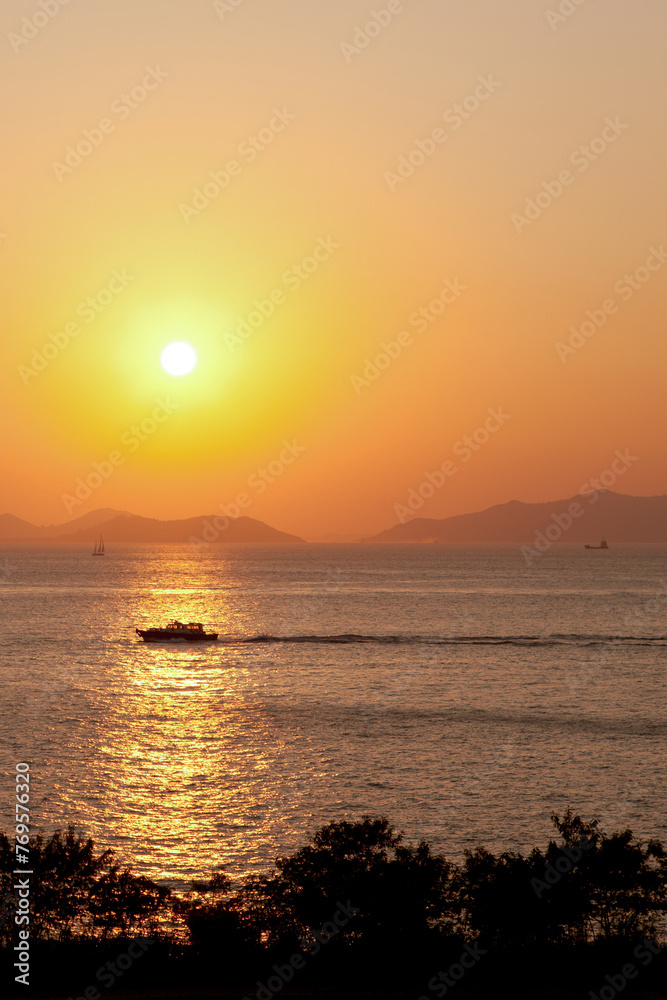 Golden Sunset Serenity. A tranquil sunset over the ocean, with a boat silhouetted against the warm hues of the sky. Calm and inspiring.