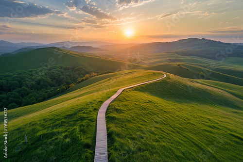 Aerial view of a path passing through beautiful green hills during the sunset