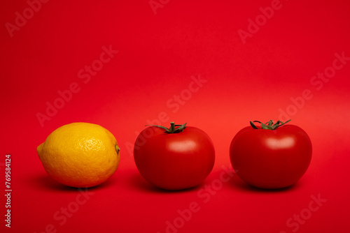 two tomatoes and lemon on a red background © Andrei