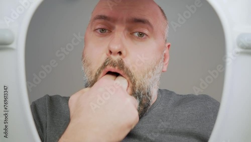 Food poisoning. Sick man vomits into toilet. Male in restroom puts fingers in mouth to induce nausea and vomiting attack. Poisoning with harmful substances and expired food with bacteria . View from