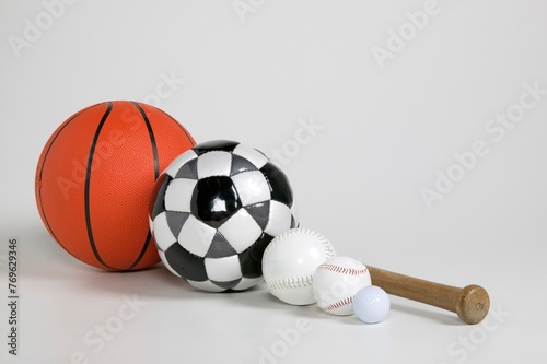A collection of sports equipment including a basketball, soccer ball, two baseballs, and a wooden baseball bat.