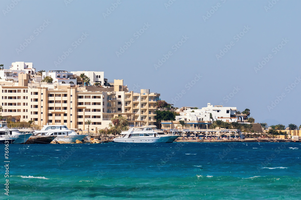 Hurghada Old Town (Egypt) as seen from sea, coast with luxury yachts foregrounding sandy-hued architecture, reflecting modern nomadic trends and serene aquamarine waters