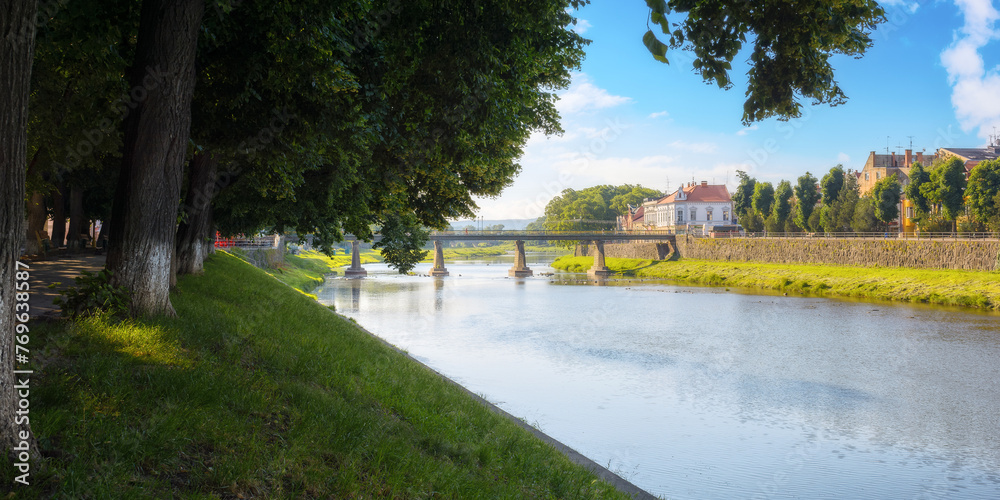 uzhgorod, ukraine - 04 jun 2017: old town with river. embankment with linden trees in blossom. bridge and old buildings in the distance in morning light uzhgorod, ukraine - 04 jun 2017: old town with river. embankment with linden trees in blossom. bridge and old buildings in the distance in morning light