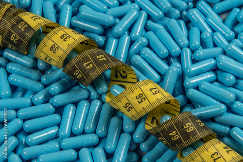 Blue weight loss pills and measuring tape symbolizing slimming photo