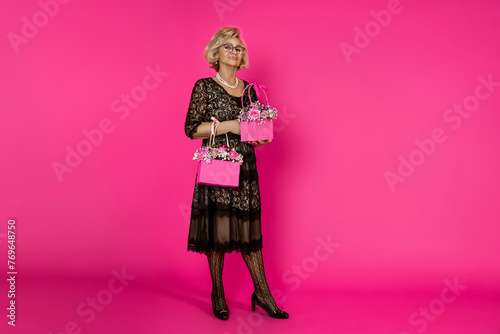 Beautiful happy senior woman in elegant black dress holding a bouquet with flowers on a pink background in the studio.Mother's Day and Grandmother's Day concept.