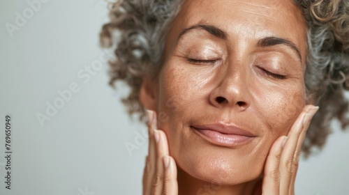 A woman with closed eyes smiling and gently massaging her face with her hands conveying a sense of relaxation and self-care.