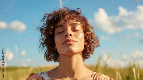 A woman with closed eyes enjoying a moment of tranquility in a field with tall grass and a clear blue sky.