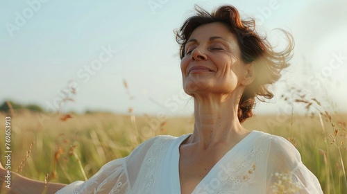 A woman in a white dress with her eyes closed smiling and enjoying the breeze in a field of tall grass.