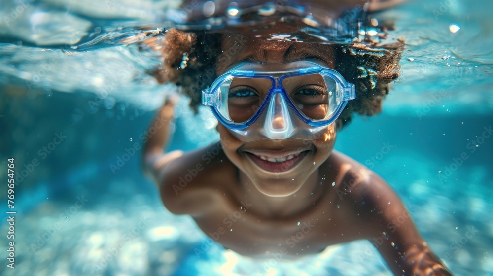 A joyful child with curly hair wearing blue goggles swimming underwater with a radiant smile.