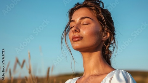 A woman with closed eyes enjoying a serene moment standing in a field with her hair blowing in the wind. photo