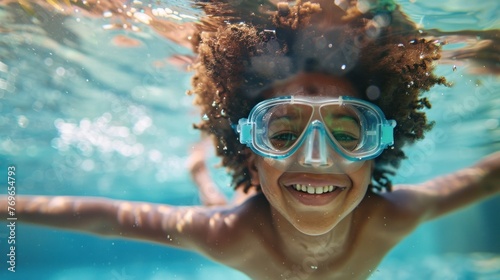 A joyful child with curly hair wearing blue goggles smiling underwater in a swimming pool.