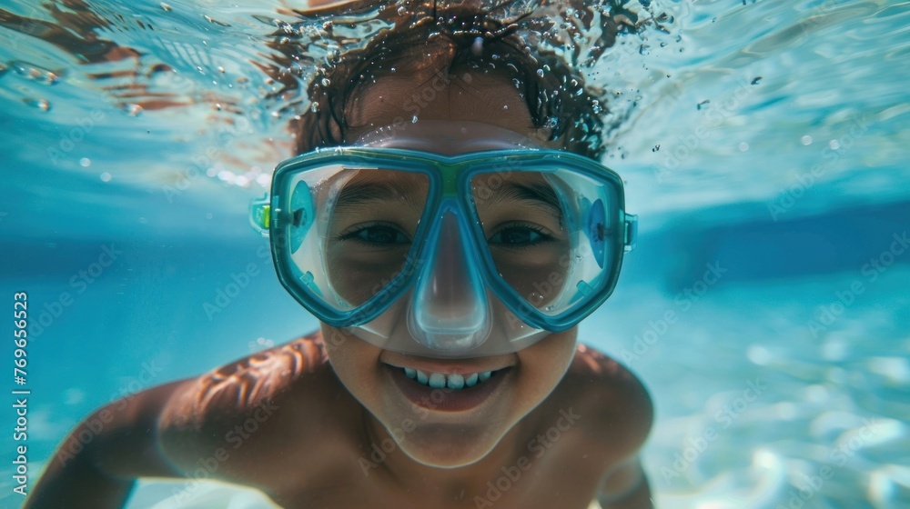 Young child underwater with blue goggles smiling in clear blue water.