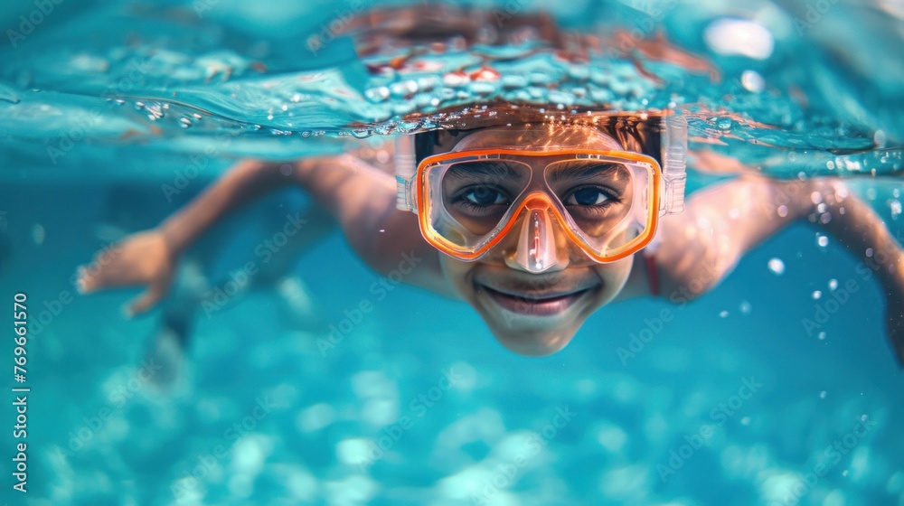 A joyful child with orange goggles smiling underwater in a pool.