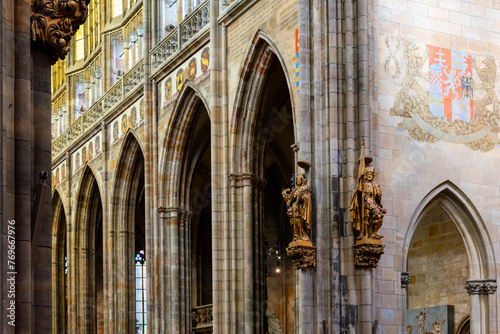 The vaulted ceilings and gothic arches of Saint Vitus Cathedrals interior are showcased, accented by heraldic banners and intricate sculptures. Prague Castle, Prague, Czechia photo