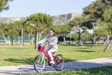 A young girl is riding a pink bike in a park