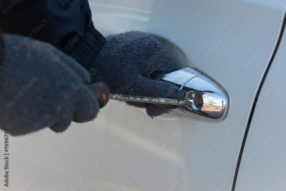 Close-up Man dressed in a black holding screwdriver to break the lock and steal a vehicle on the road, Social destruction, Insurance, Car thief concept. - obrazy, fototapety, plakaty 