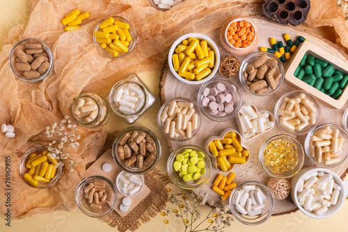 Big amount of various dietary supplements pills, vitamins, minerals, tablets and capsules in small jars from above on a wooden desk on beige background in rustic style.