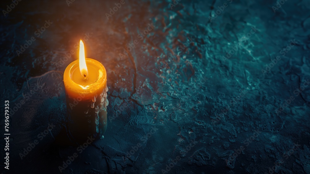 Fototapeta premium A single lit yellow candle on a textured blue surface with soft lighting.
