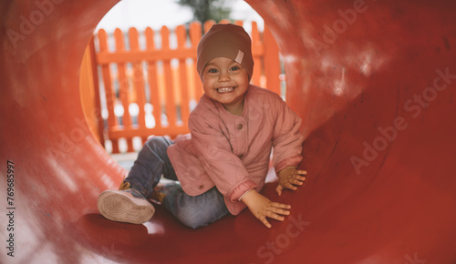 Smiling toddler girl playing in the playground's tunnel or tube