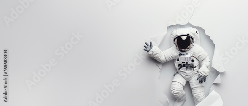 An astronaut in a spacesuit appears to be breaking through a plain white wall, giving a sense of discovery or breakthrough