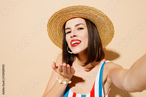 Close up young woman in one-piece swimsuit straw hat near hotel pool do selfie shot pov on mobile cell phone blow air kiss isolated on plain beige background Summer vacation sea rest sun tan concept