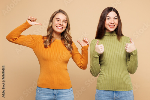 Young friends two women they wear orange green shirt casual clothes together point index finger on themselves show thumb up isolated on plain pastel light beige background studio. Lifestyle concept.