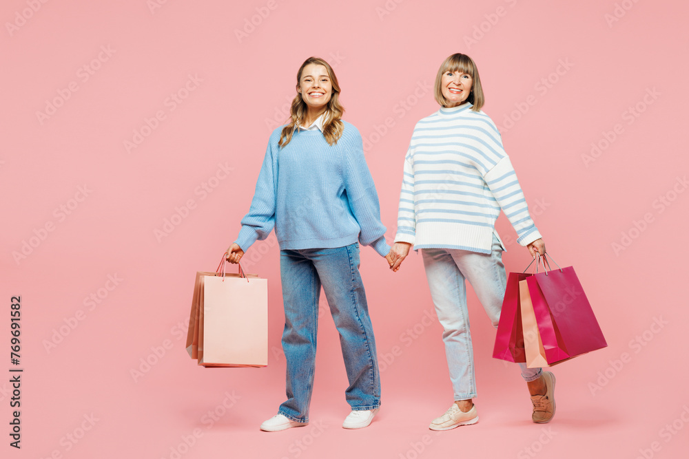 Full body elder parent mom young adult daughter two women together wear blue casual clothes hold paper package bags after shopping isolated on plain pink background Black Friday sale buy day concept. Full body elder parent mom young adult daughter two women together wear blue casual clothes hold paper package bags after shopping isolated on plain pink background Black Friday sale buy day concept.