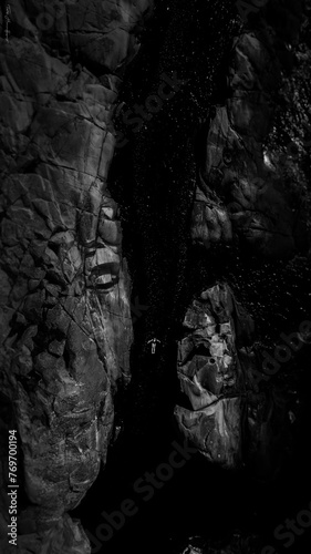 Black and white picture of rocks around a river with a person floating in the water