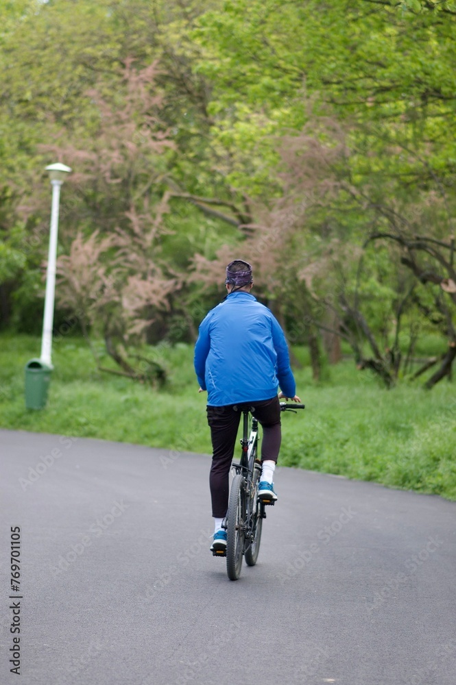Young adult cyclist leisurely riding a bicycle down a rural road surrounded by trees