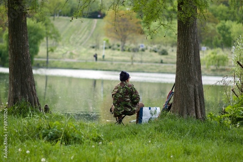 a man sitting under some trees by a pond fishing