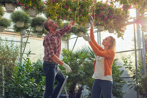 Man and woman working in a flower nursery greenhouse, taking car