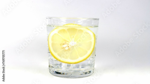 Freshly cut lemon submerged in glass of alcoholic drink on white background