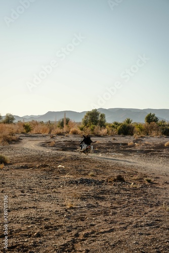 Young adult in protective gear riding a dirt bike along a desert trail