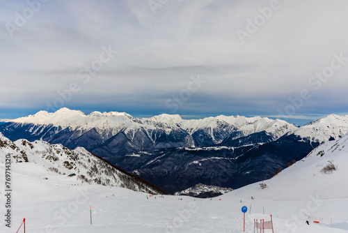 Mountain scenery to snowy peaks from the ski slope with fluffy clouds in the blue sky. Overcast. Copy space.