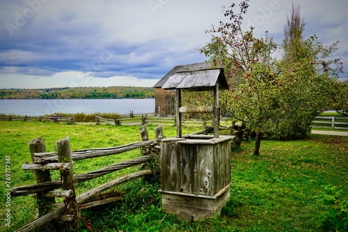 Aged wishing well in a lush green meadow, with a wooden fence in the background photo