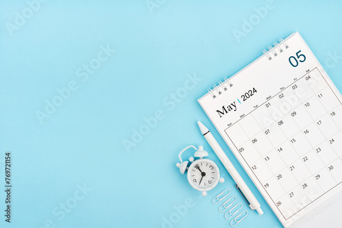 May 2024, Monthly desk calendar for 2024 year and alarm clock with paper clips on blue color background.