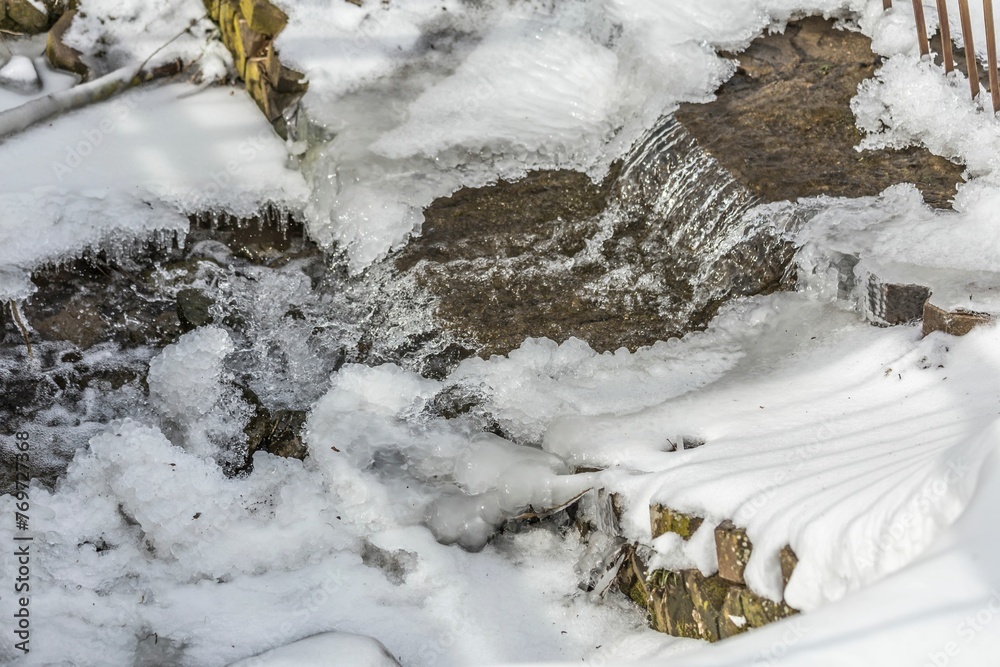 Scenic view of a small waterfall cascading over rugged rocks, covered in a layer of frosty snow