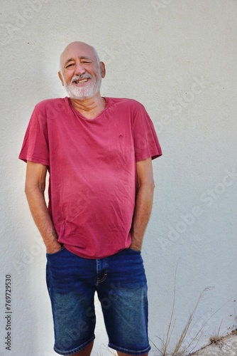 Happy mature elderly man wearing pink shirt and standing against white wall