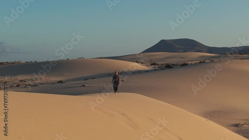 woman walking up a sand dune at sunset