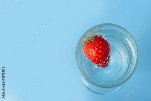 A glass glass with water and red ripe strawberries isolated on a blue background, top view. Summer is a healthy drink. Summer cocktail. © Alena