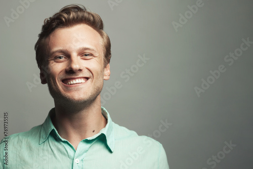 Male beauty, boy next door concept. Portrait of laughing 30-year-old man standing over gray background. Close up. Classic style. Wavy glossy blond hair. Copy-space. Studio shot