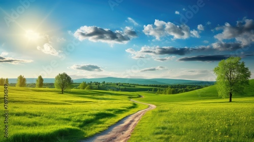 Picturesque winding path through a green grass field in a hilly area in the morning at dawn against blue sky with clouds. Natural panoramic spring-summer landscape.