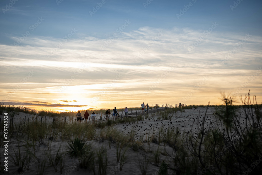 Group of people walking along a sandy beach silhouetted against a beautiful sunset.