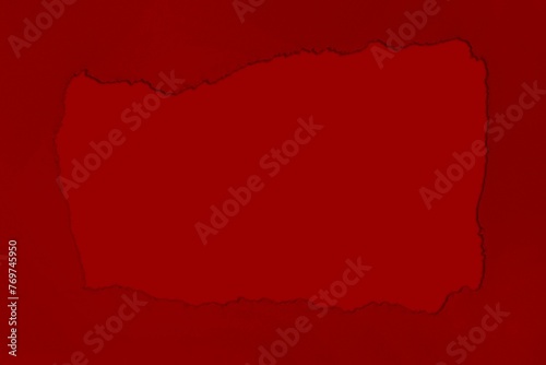 Red torn cardboard piece isolated on a burgundy background, illuminated by natural light