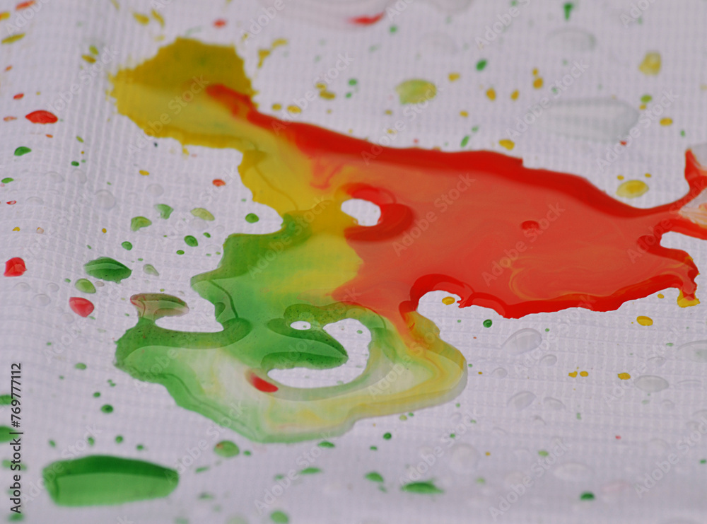 splashes of ink or paint on the surface of a shiny material. drops on the surface of the tarpaulin are green, red and yellow mixed with water. wet glossy banner material
