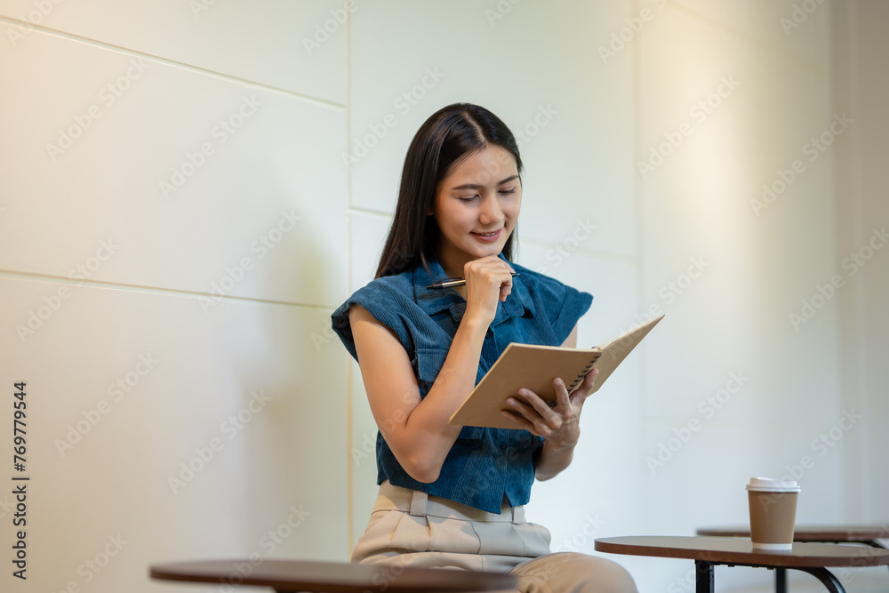 Smiling young woman engrossed in writing notes in a notebook in a café with a takeaway coffee cup on the table. Smiling young woman engrossed in writing notes in a notebook in a café with a takeaway coffee cup on the table.