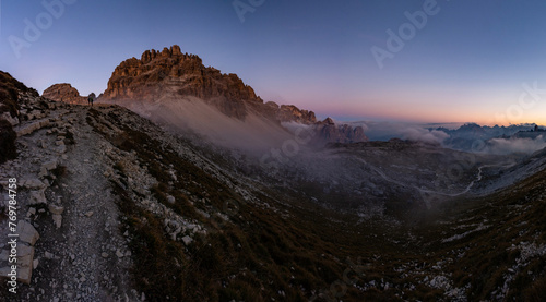 Panoramic photo of Paternkofelnext to the famous Tre Cime peak in the Italian Dolomites during the blue hour after the sunset with a couple taking selfie photos of themself in the pass 