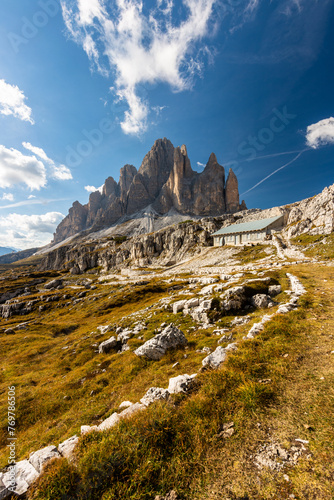 Rocky footpaths below the monumental peak of Tre Cime with the cloudy blue sky