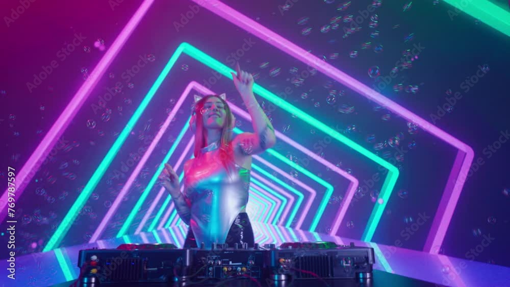 Attractive female on digital wall colorful visual graphic background. Young woman dj dancing, plays music on turntables mixer at night club, looks at camera.